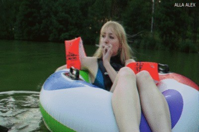 Alla is swimming in an inflatable ring on the lake and Smoking a cigarette.